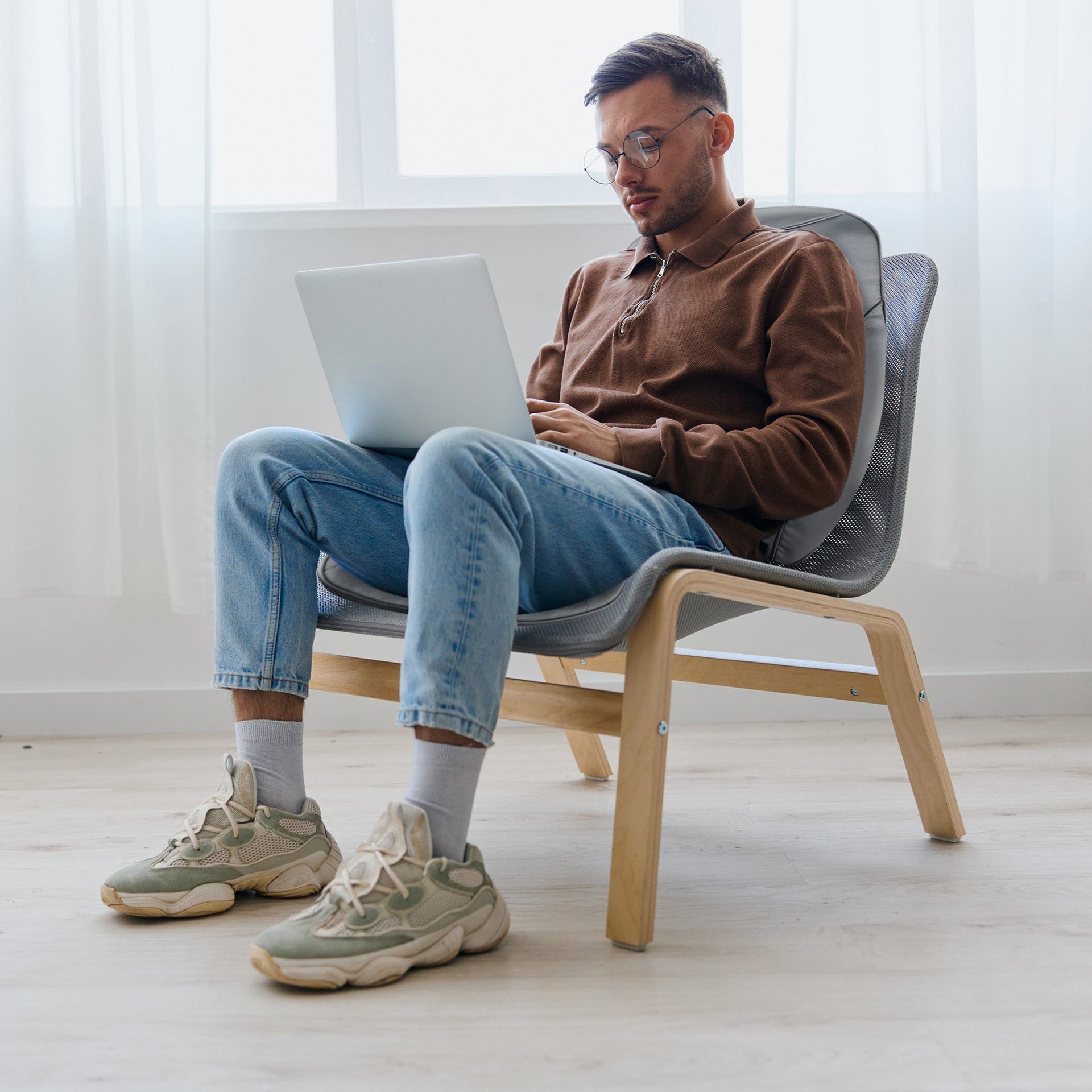Man sitting on a chair using a laptop in a bright room.