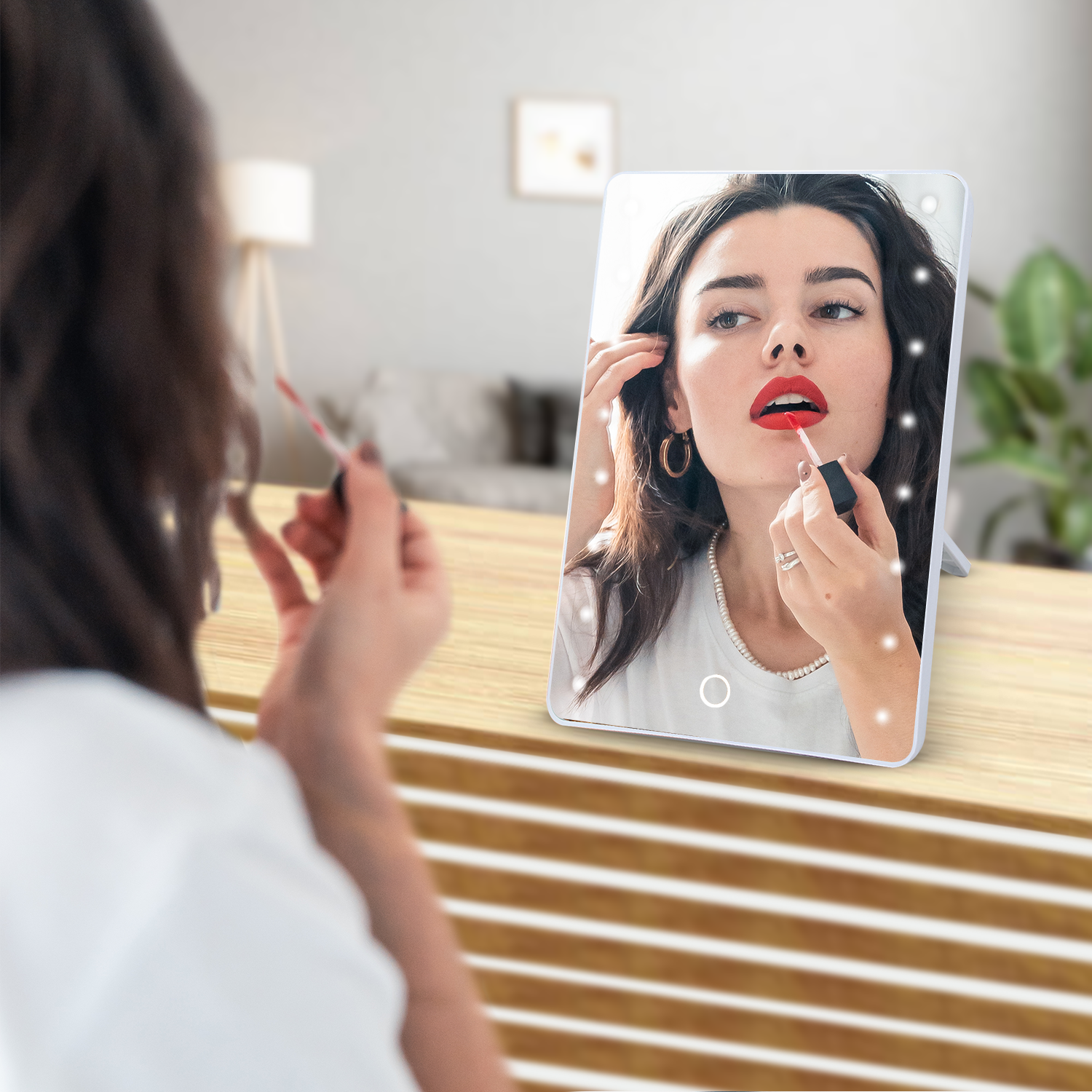 Woman applying lipstick in front of a smart mirror with LED lights.