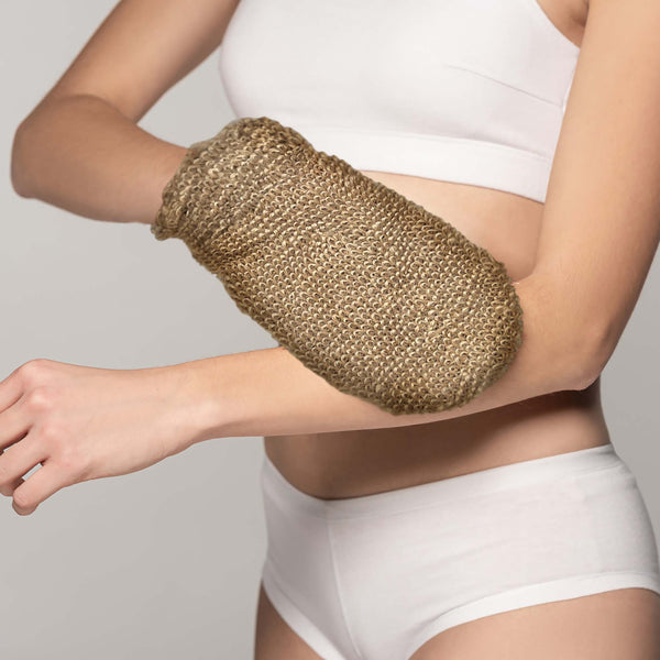 Person wearing a gold exfoliating glove on one arm against a neutral background