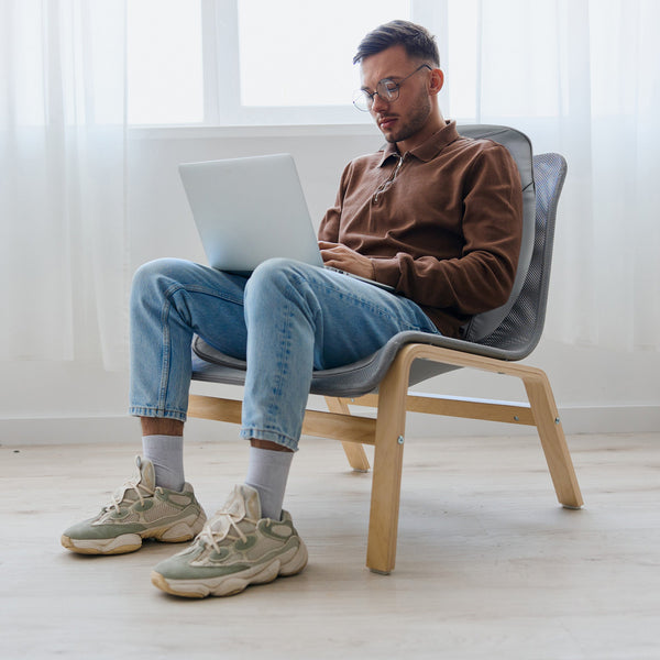 Man sitting on a chair using a laptop in a bright room.