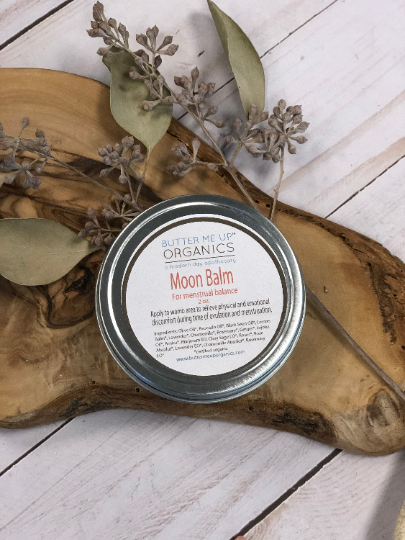 ointment in a tin container on a slab of wood with plants around it