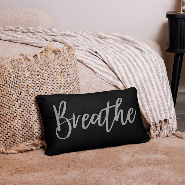 black pillow with the word breathe written on it propped next to a bed