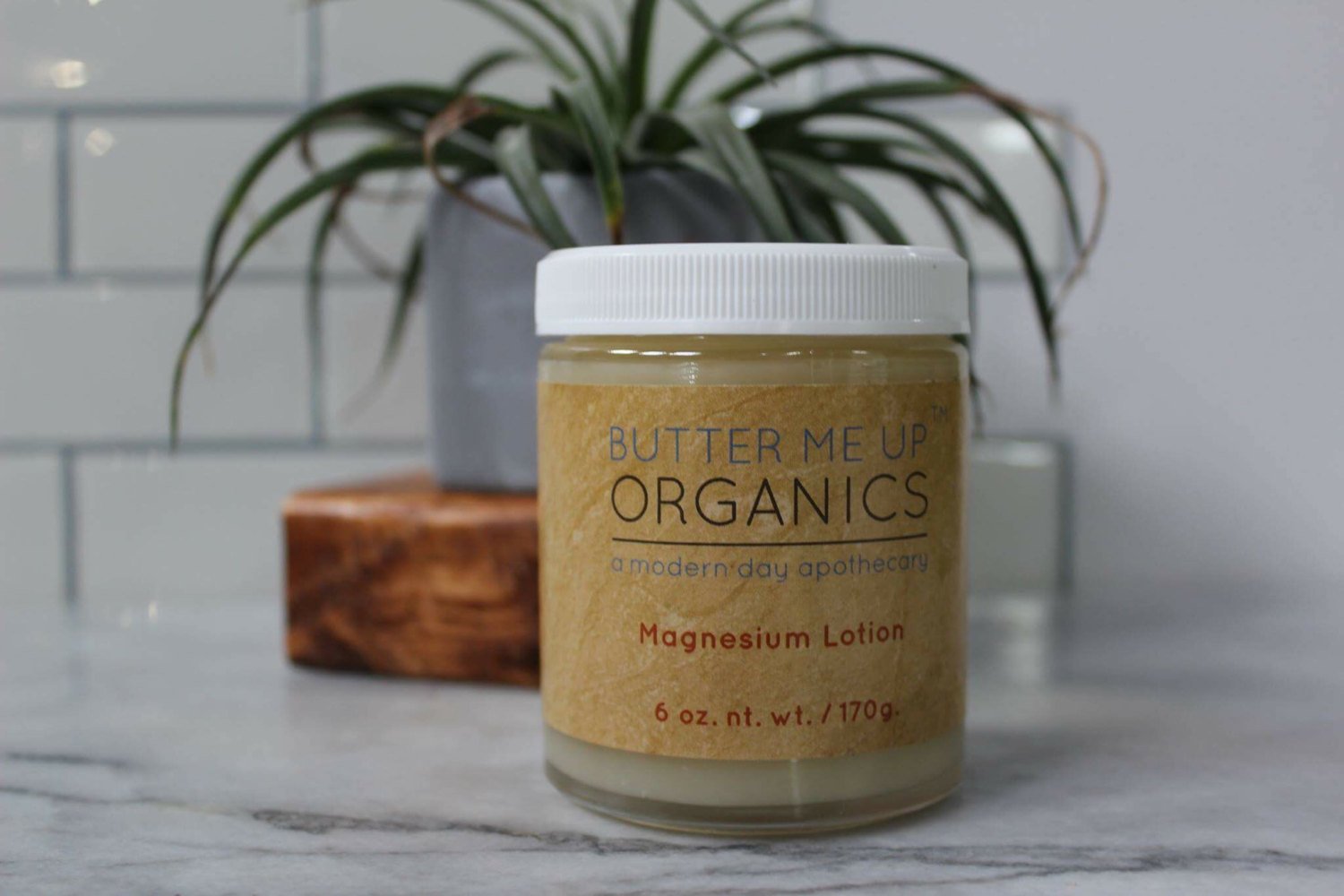 butter me up organics magnesium lotion on a shelf with decorative plants surrounding it