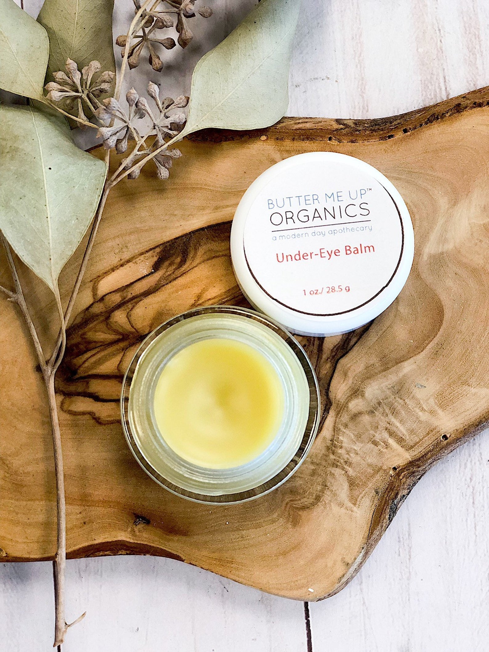 glass jar of butter me up organics under eye balm on top of a wooden slab