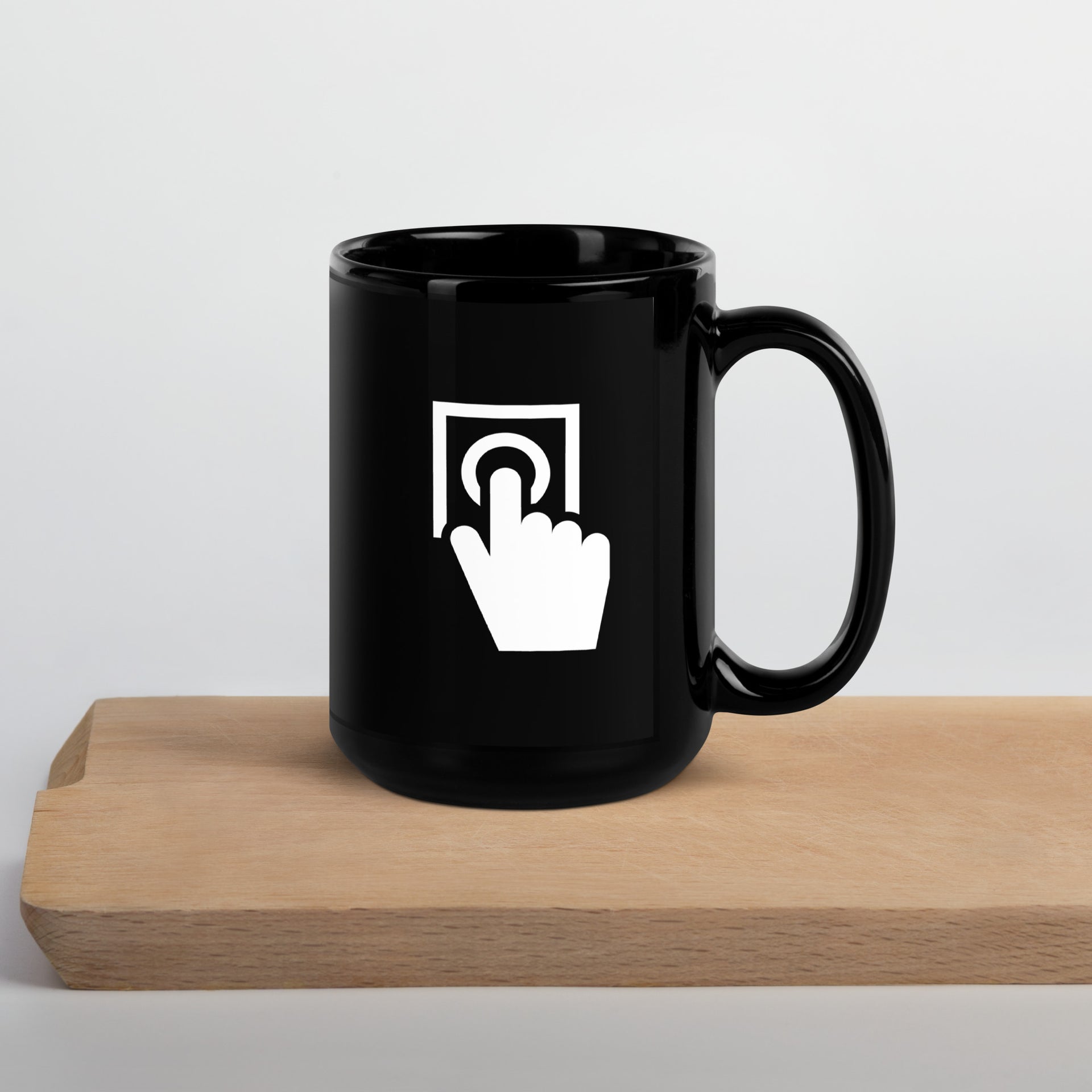 black coffee mug with a picture of a button and a hand pushing the button printed on the cup, cup is sitting on top of a piece of wood