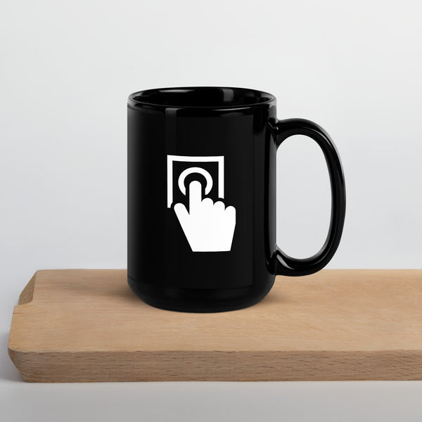 black coffee mug with a picture of a button and a hand pushing the button printed on the cup, cup is sitting on top of a piece of wood